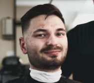 A caucasian man with a beard smiling at the camera during his haircut