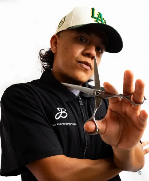 Barber Gerson is wearing a baseball cap while posing with his haircutting scissors
